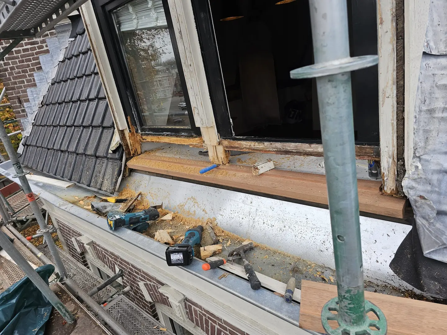 Een raam met een volledig rot kozijn waarvan een deel is weggeslepen om hersteld te worden